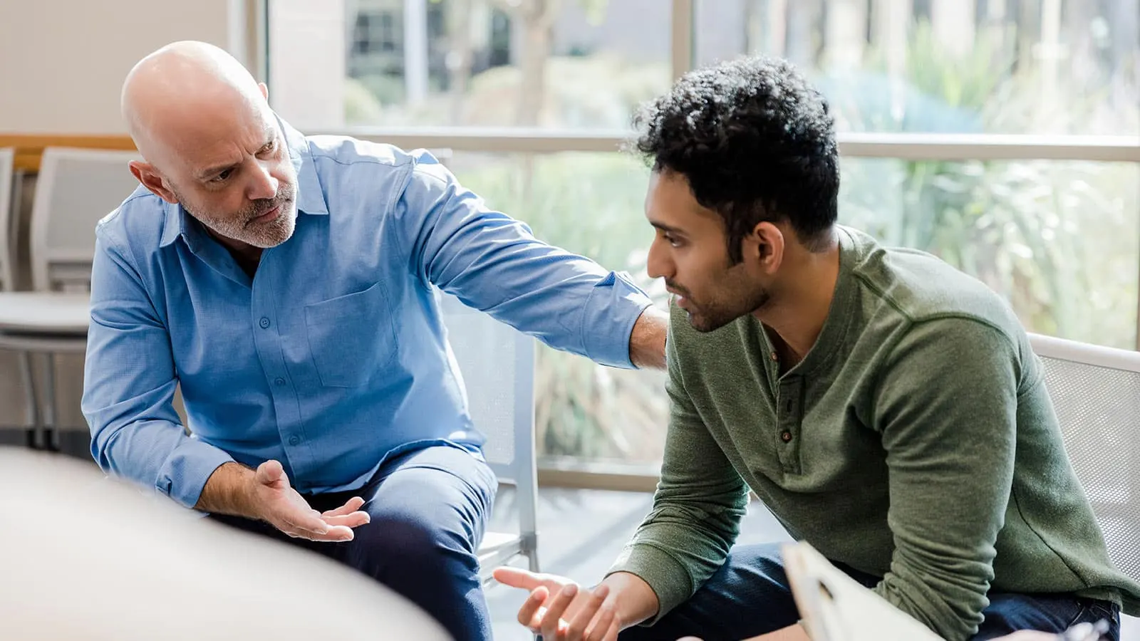 A counselor in a blue shirt reaching out while talking with a young man during a session