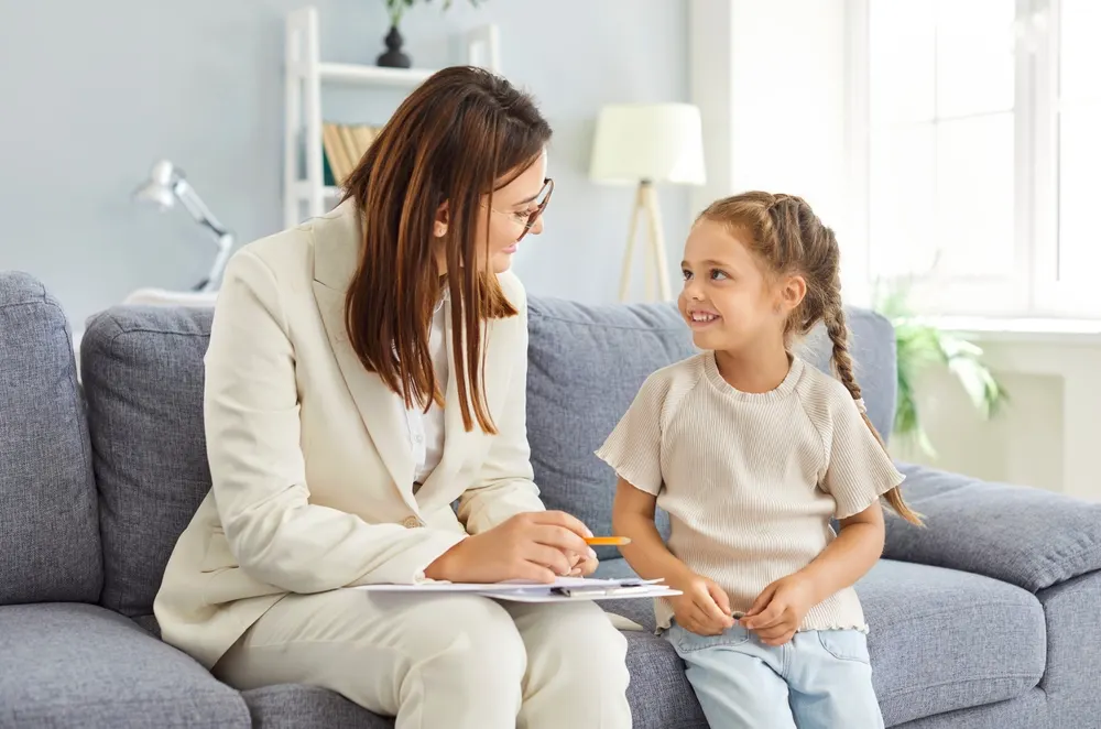 A counselor with a clipboard smiling at a young girl seated beside her on a sofa