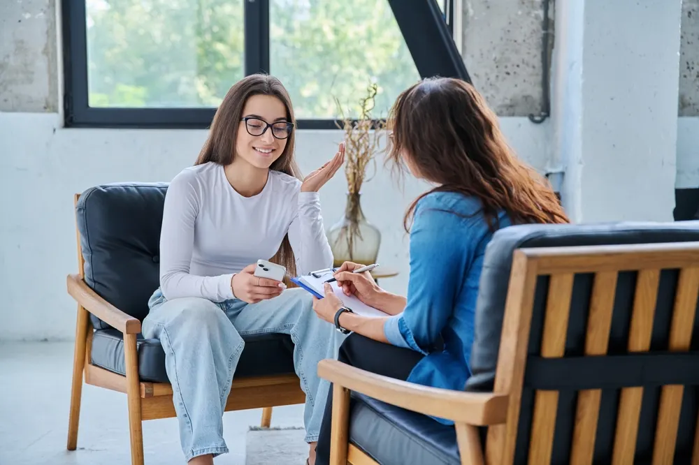 A counselor writing on a clipboard while a young client speaks during a session