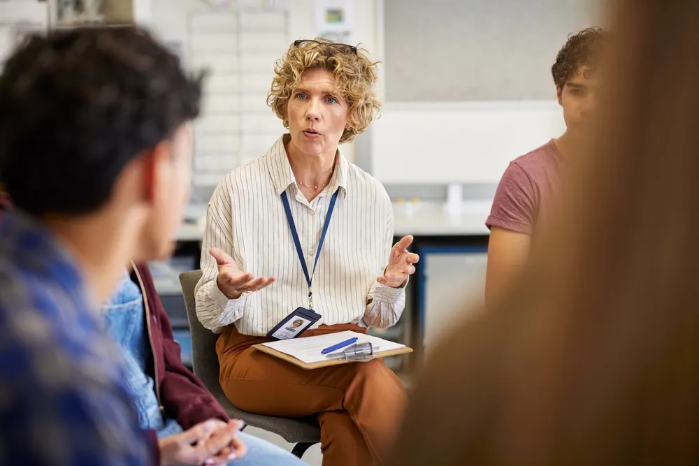 An instructor with a clipboard speaking to a seated group during a counseling class