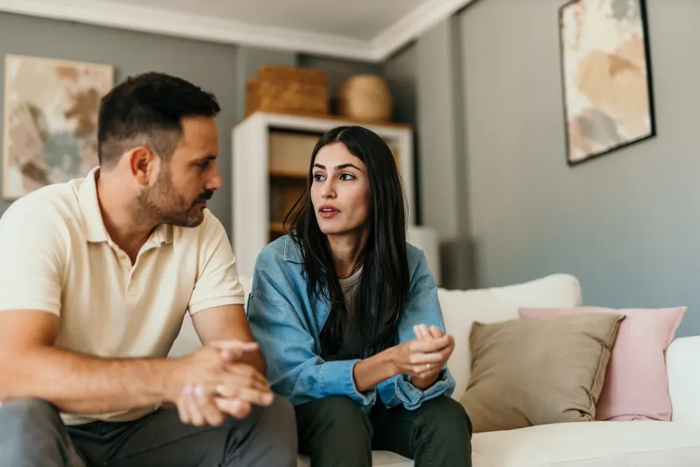 A couple sitting on a sofa during a counseling session, the woman speaking while the man listens