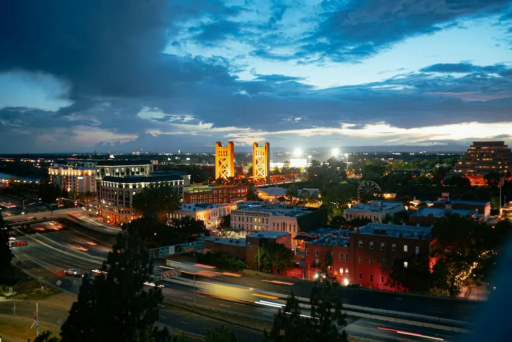 The Sacramento skyline and Tower Bridge lit at dusk above the freeway